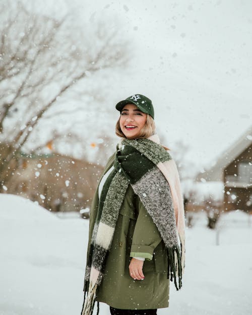 A woman in a green coat and hat smiles in the snow