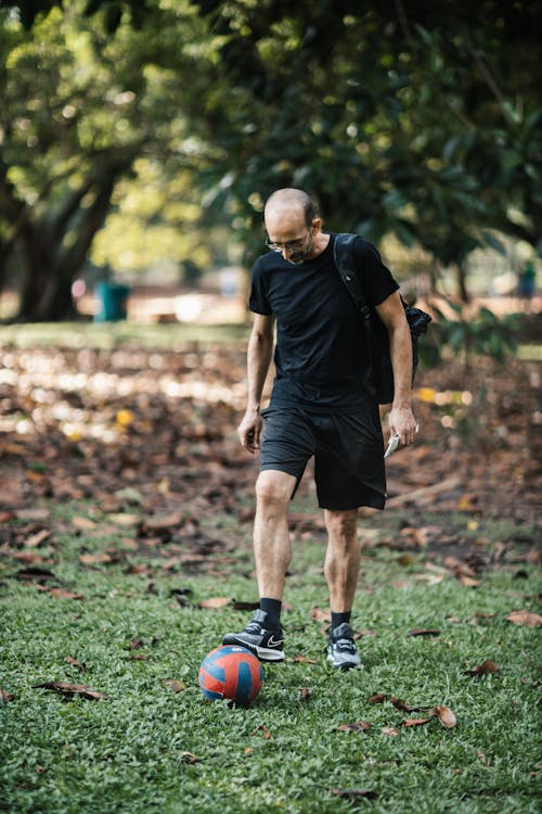 A man in black shirt and black shorts kicking a soccer ball