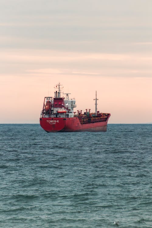 A red ship in the ocean with a pink sky