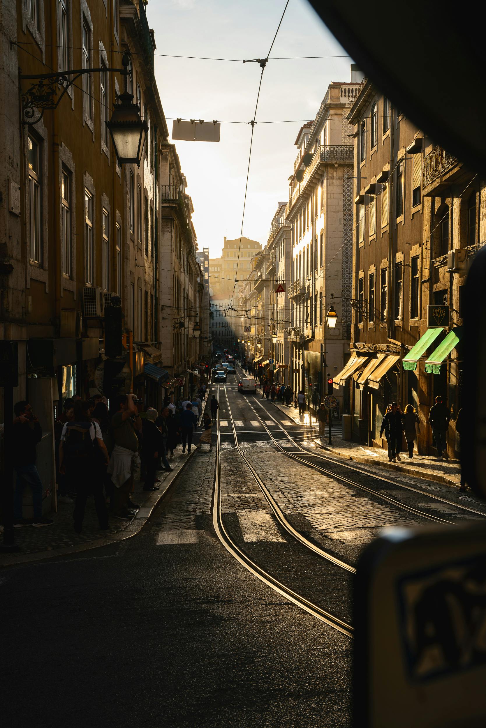 View of a vibrant Lisbon street at golden hour with bustling activity and architectural charm.