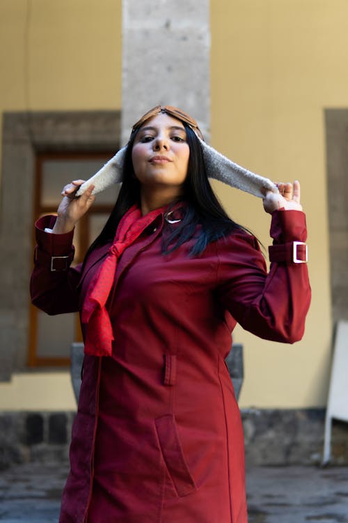 A woman in a red coat and scarf is holding her head