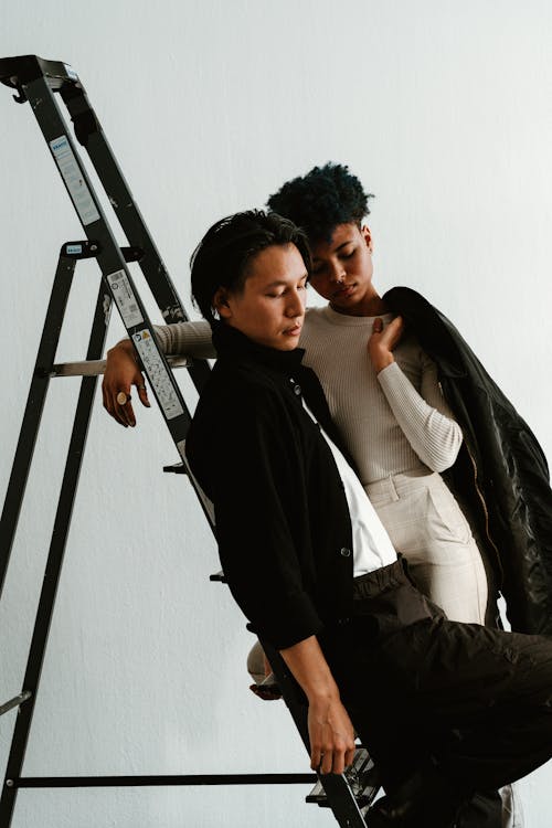 Two people sitting on a ladder, one is wearing a jacket