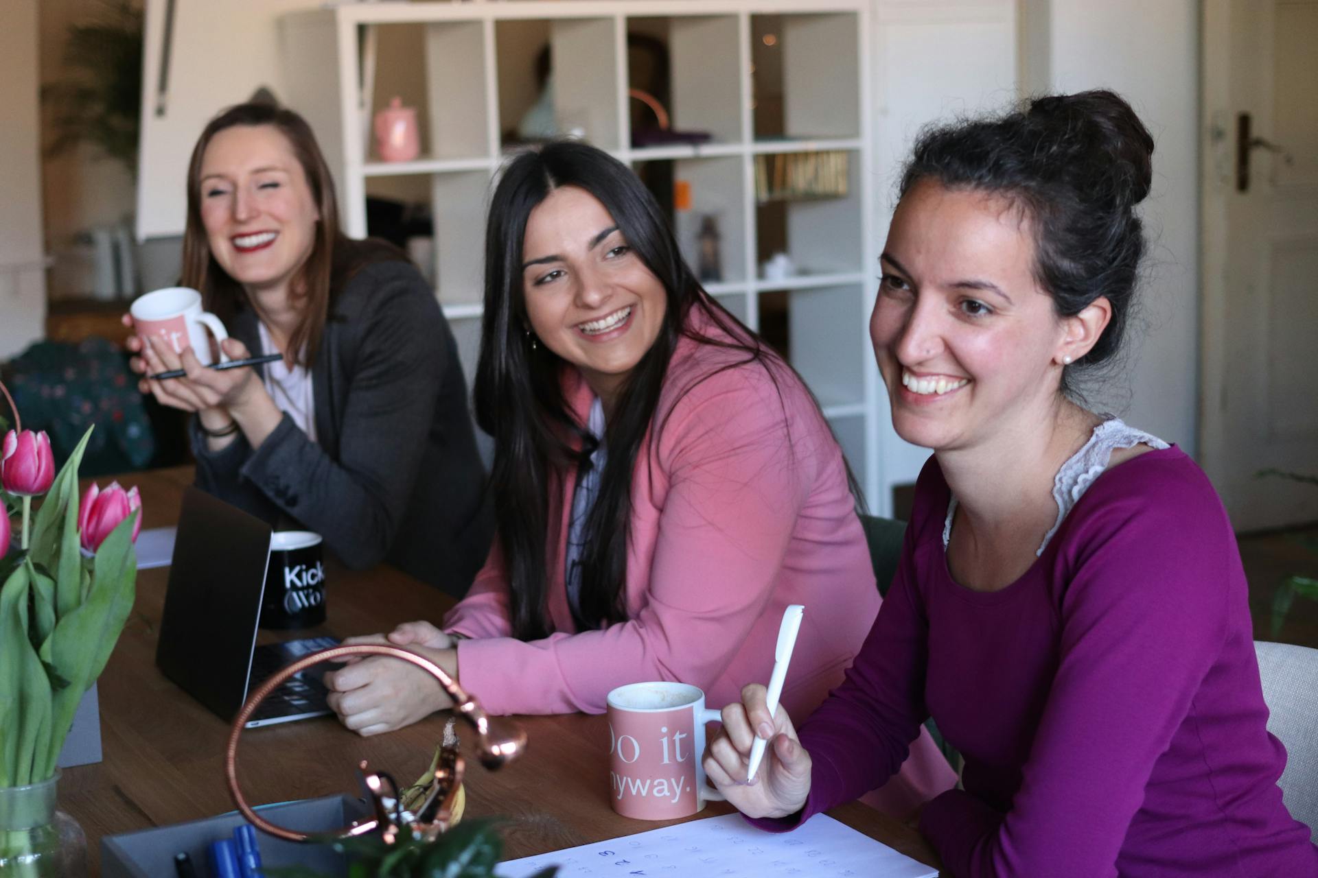 Three women enjoying a collaborative and friendly workplace meeting indoors.