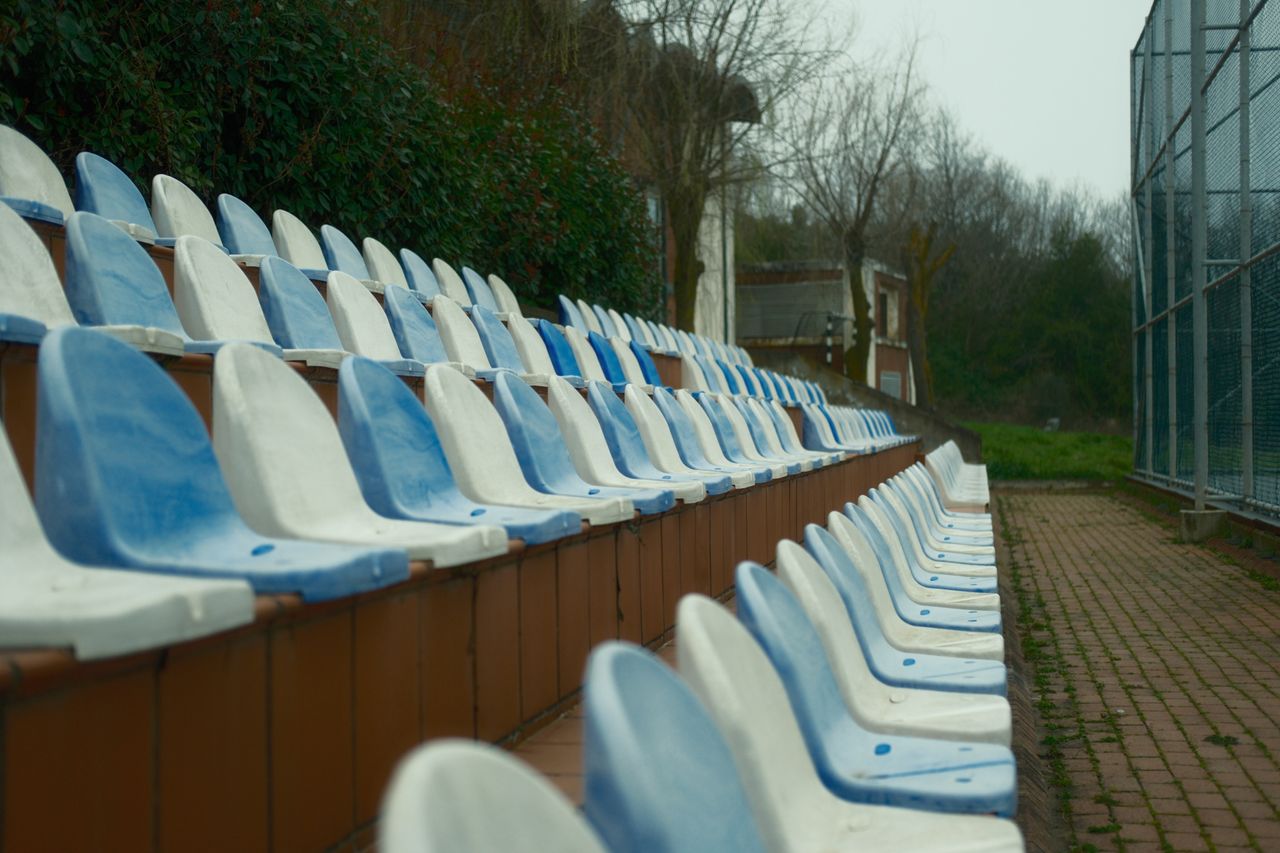 row of empty blue and white stadium seats outdoors in an overcast sett