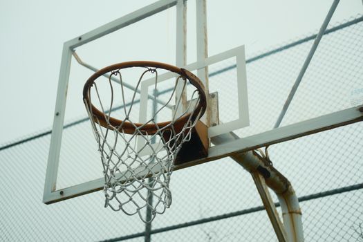 Close-up of an outdoor basketball hoop against a chain-link fence and overcast sky.