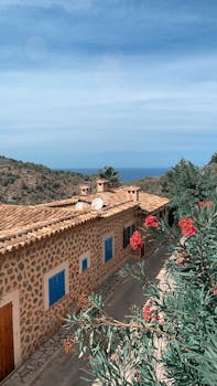Picturesque view of a stone village house in Spain with vibrant flowers and sea in the background.