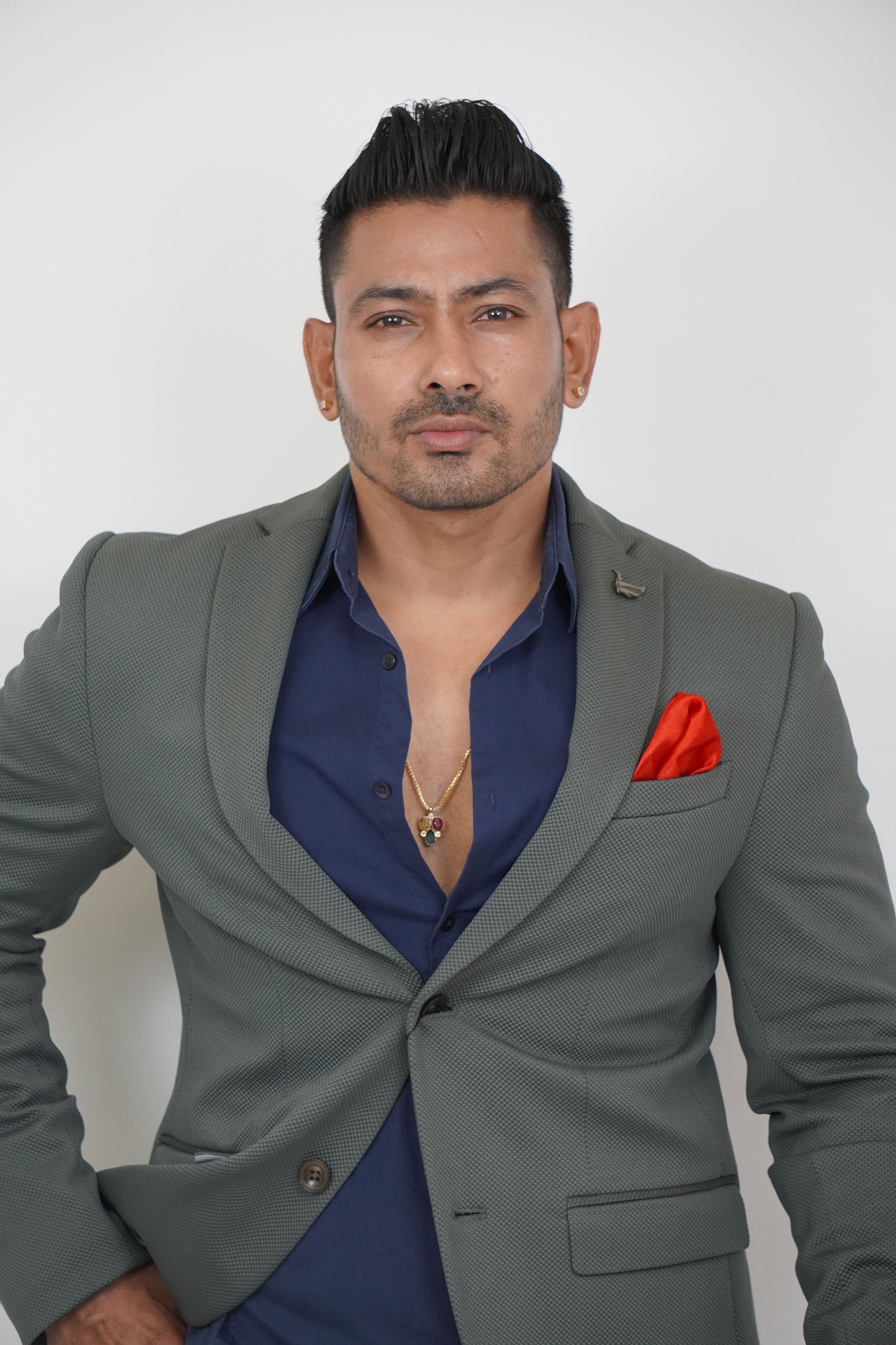 Confident man in a gray suit with red pocket square posing in a studio setting.