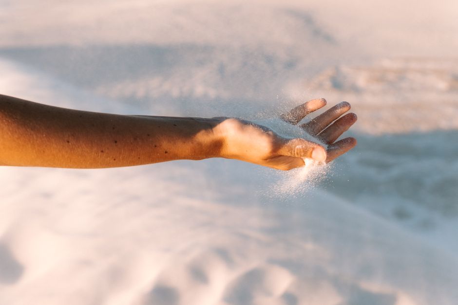 A close-up of a hand sifting sand in Lancelin Desert, Australia, captured during sunset.