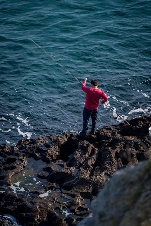 A man is fishing on the rocks near the ocean
