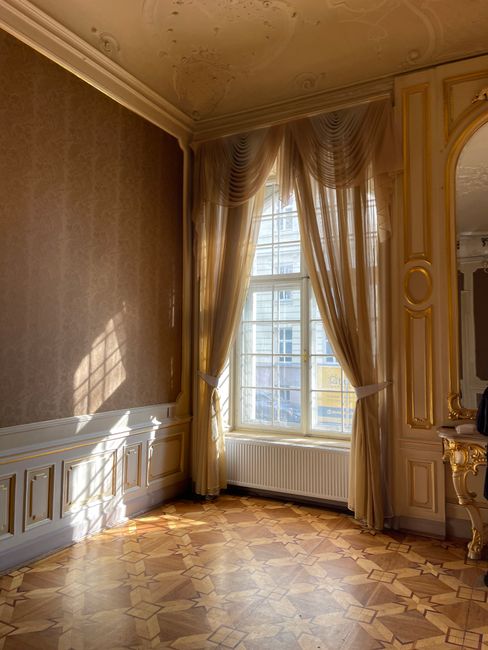 Sunlight streaming through a window in a richly decorated palace interior with vintage curtains.
