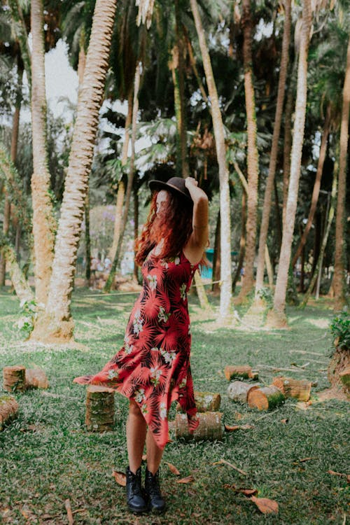A woman in a red dress and hat standing in the middle of a palm tree