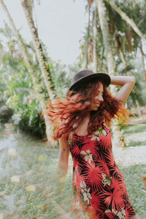 A woman with red hair and a hat is walking through a tropical area