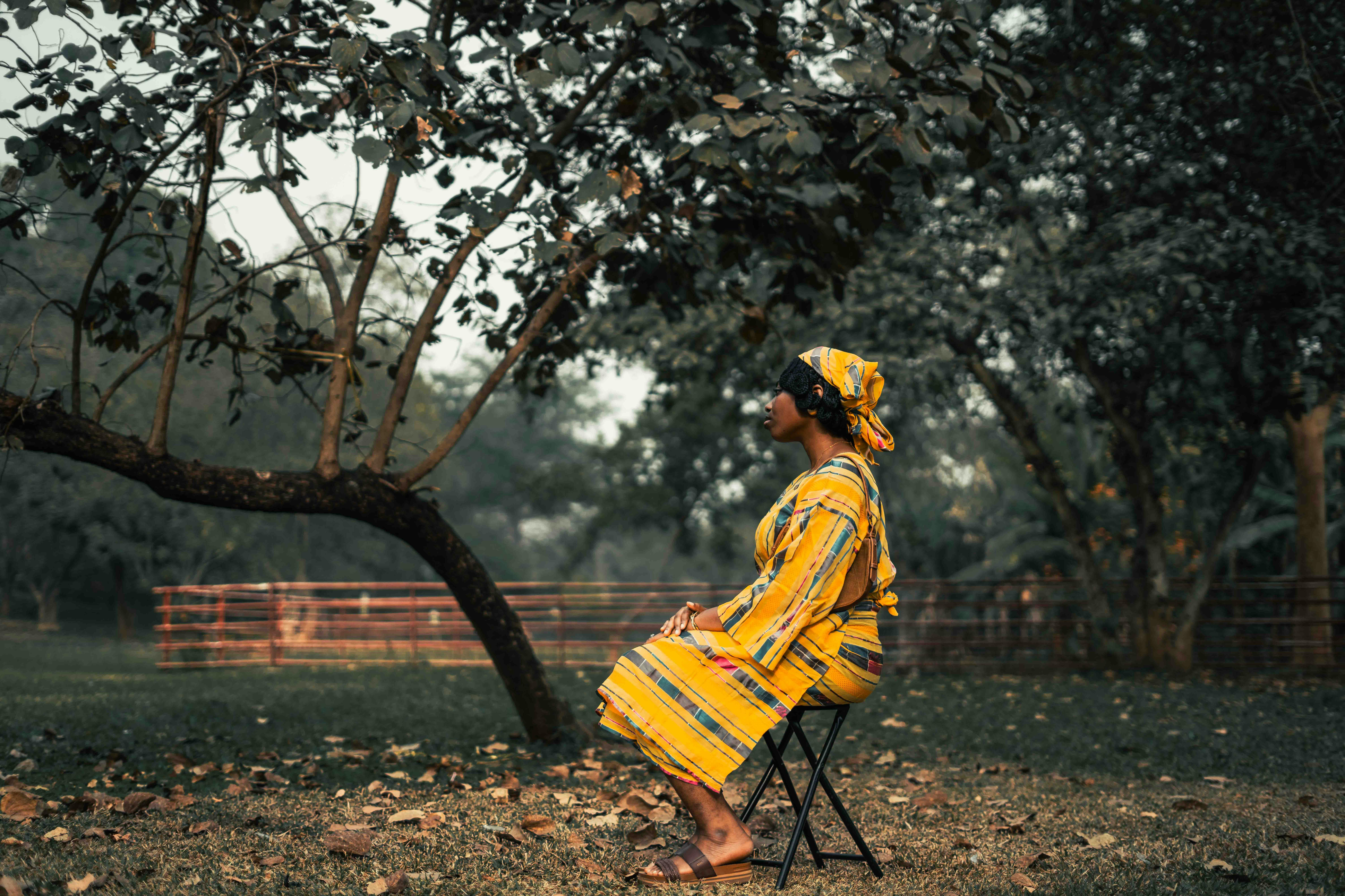 A stylish African woman in a yellow dress sitting outdoors against a natural backdrop.
