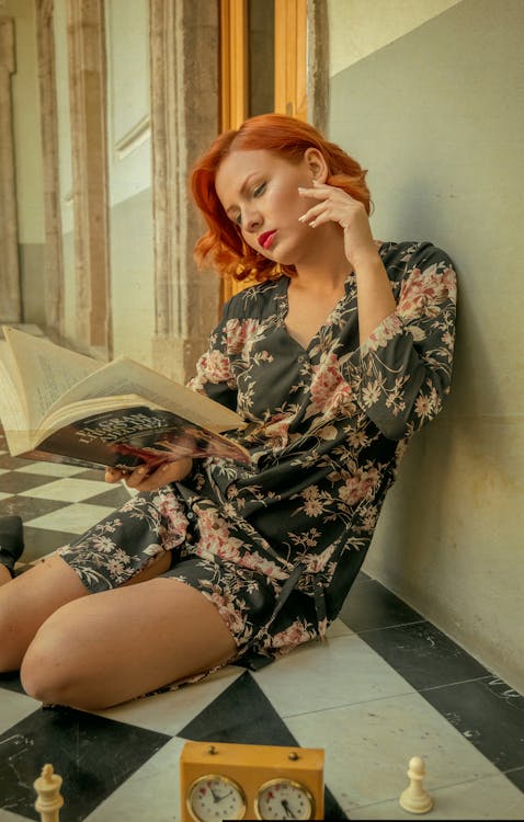 A woman reading a book while sitting on a chess board