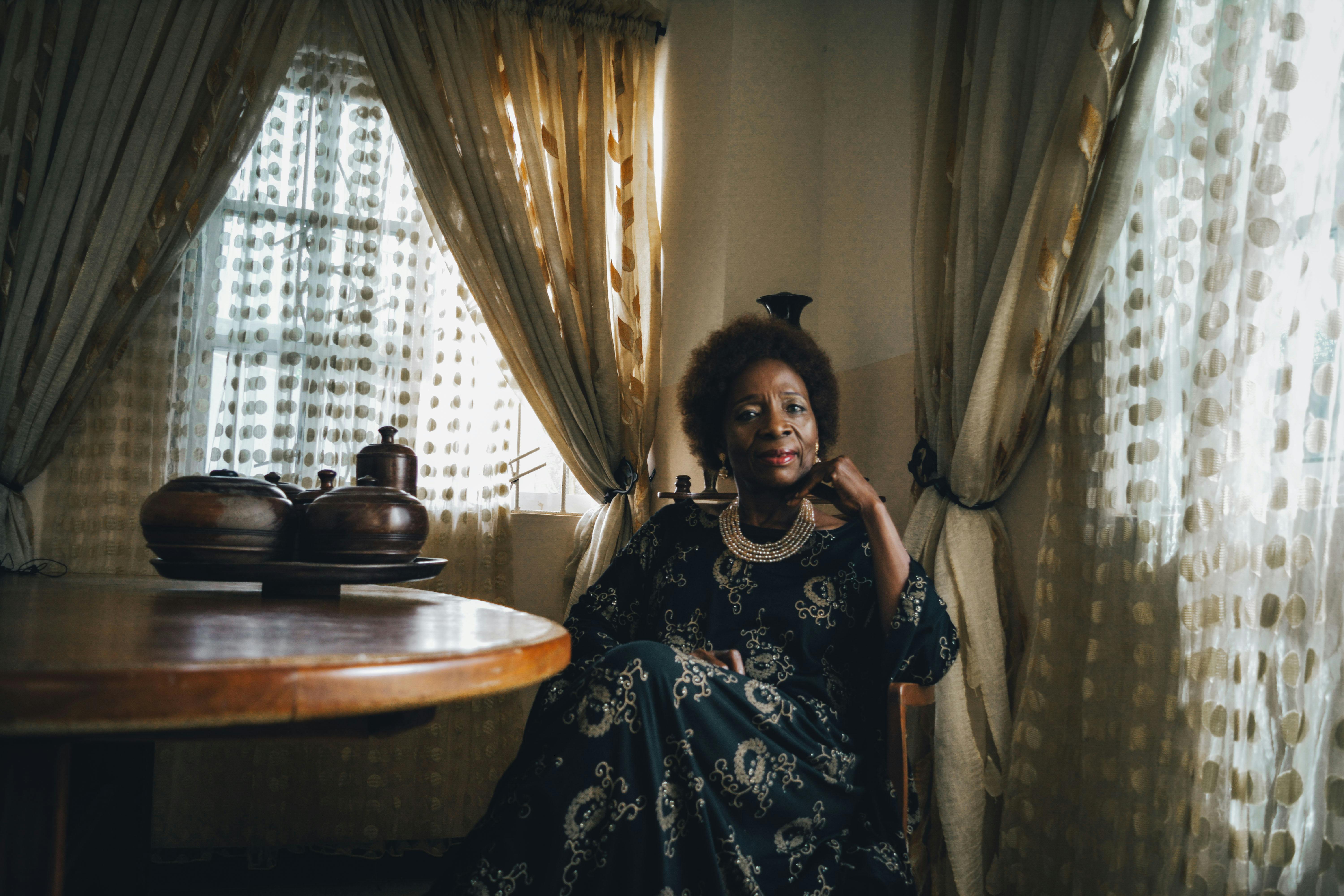 A stylish woman in an elegant black dress sits gracefully indoors, exuding sophistication and poise.
