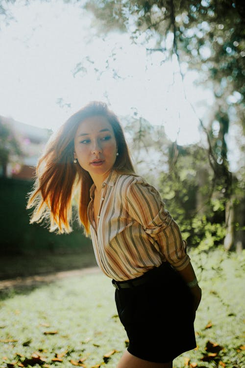 A woman in shorts and a striped shirt posing in the grass