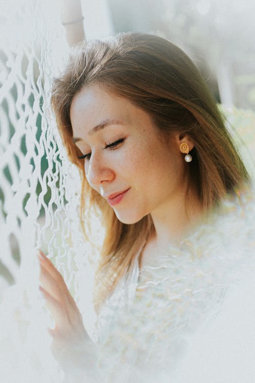 A woman looking at a window with a white lace curtain