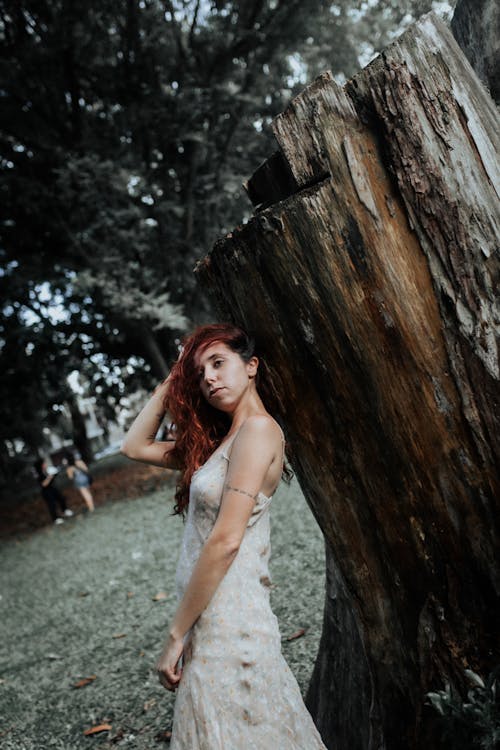 A woman in a wedding dress standing next to a tree stump