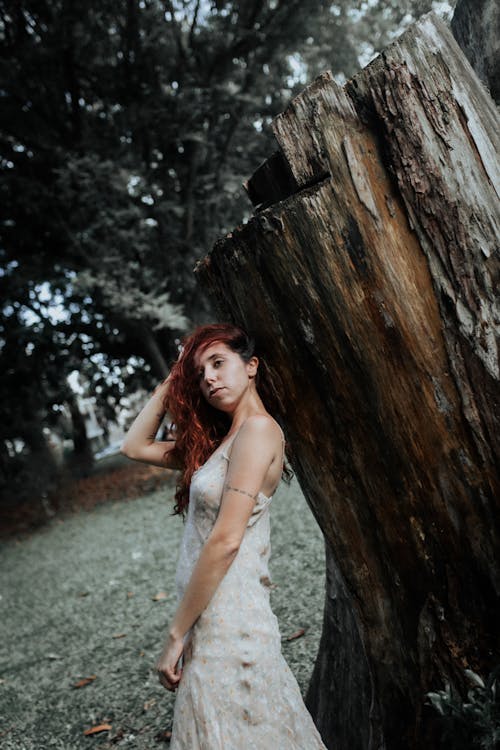 A woman in a wedding dress standing next to a tree stump