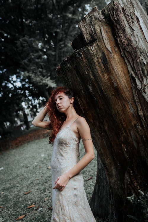 A woman in a wedding dress standing next to a tree stump