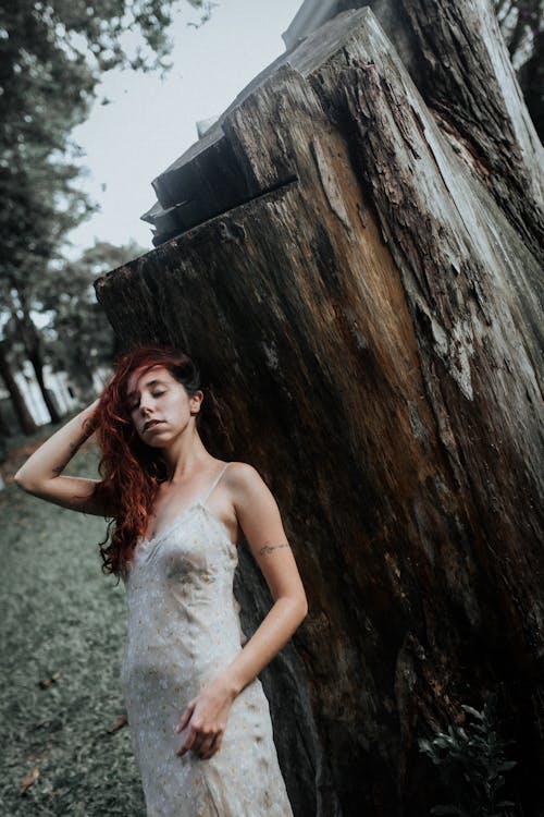 A woman in a white dress standing next to a tree stump