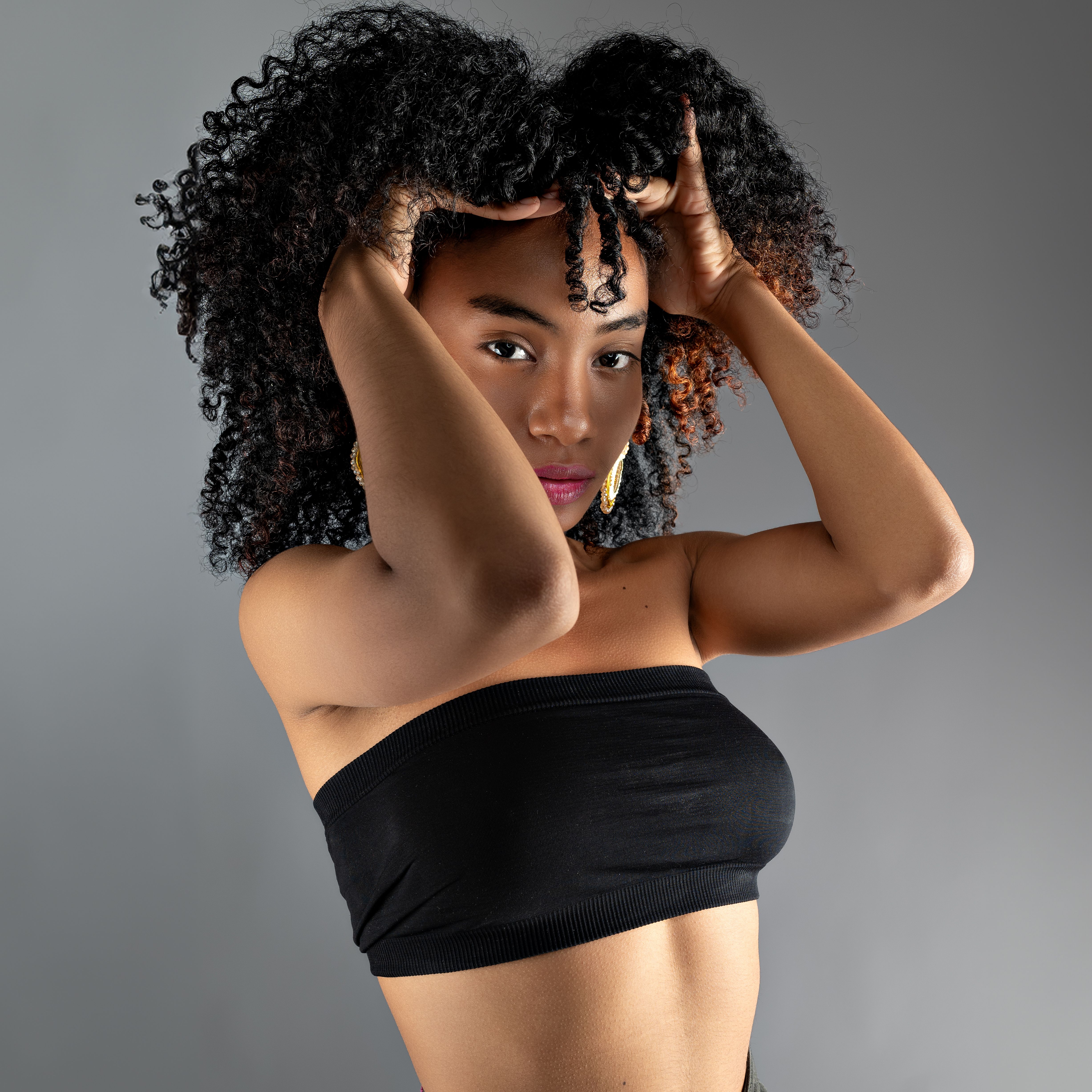 A stylish portrait featuring a young woman with curly hair posing confidently in a studio setting.