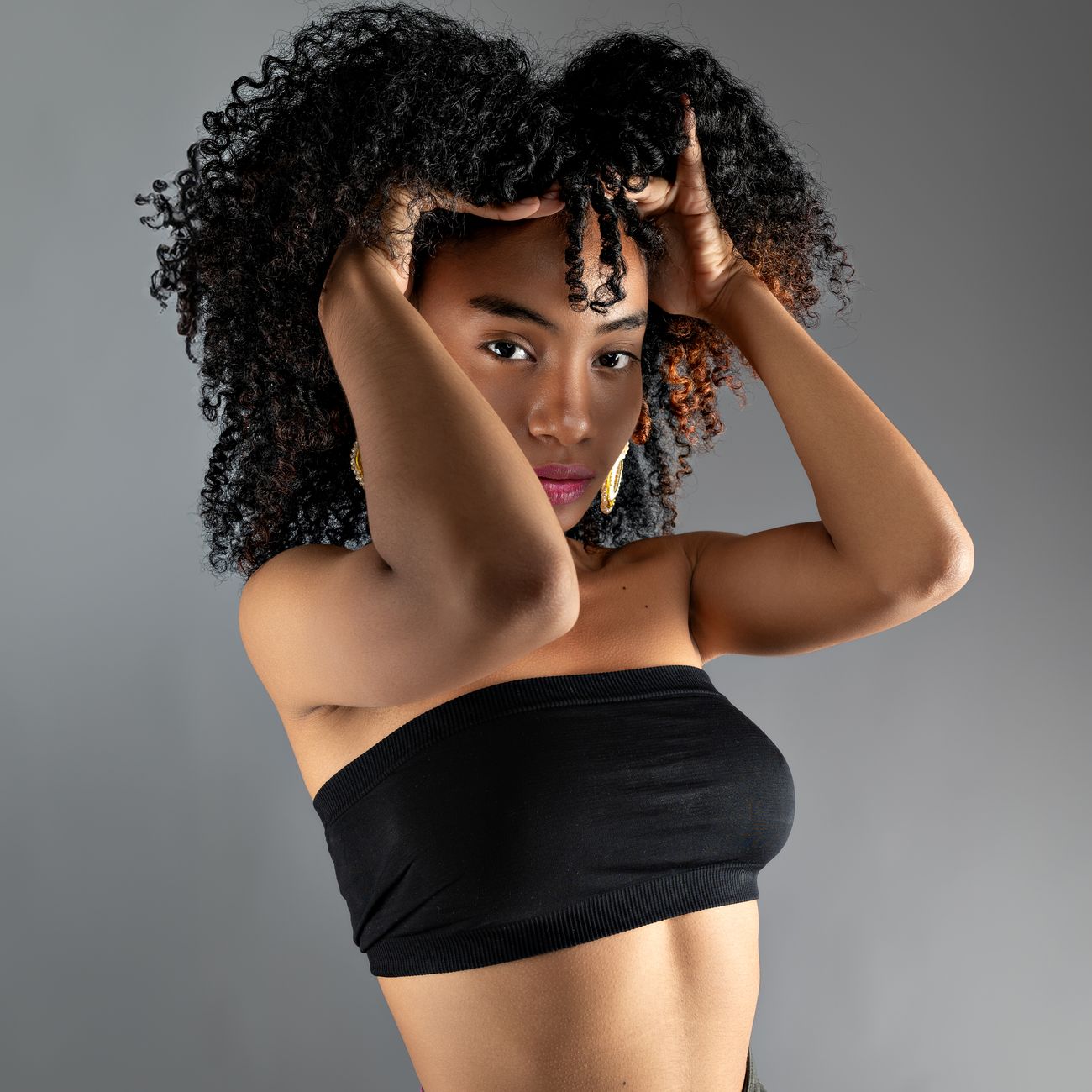 A stylish portrait featuring a young woman with curly hair posing confidently in a studio setting.