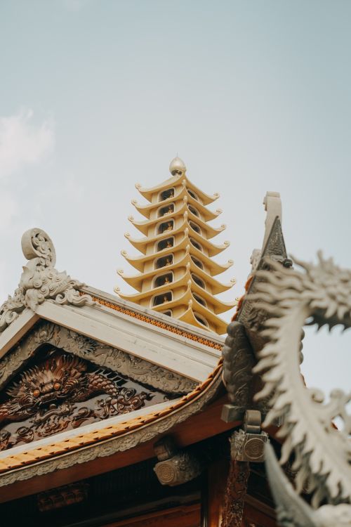 Free Close-up of a traditional ornate pagoda roof showcasing detailed carvings with a clear blue sky backdrop. Stock Photo