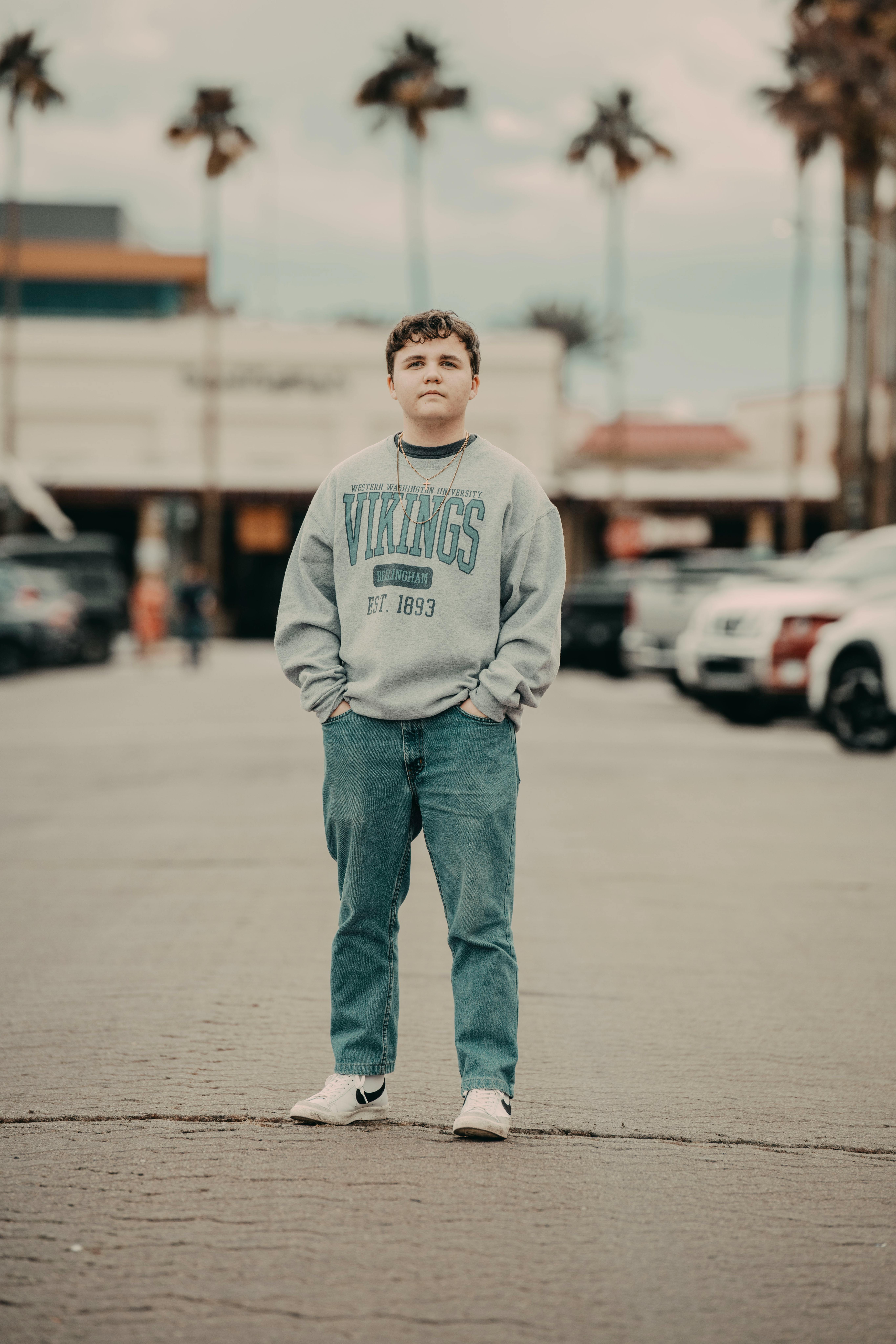 Teenager standing confidently on a city street in casual attire with hands in pockets, urban backdrop.