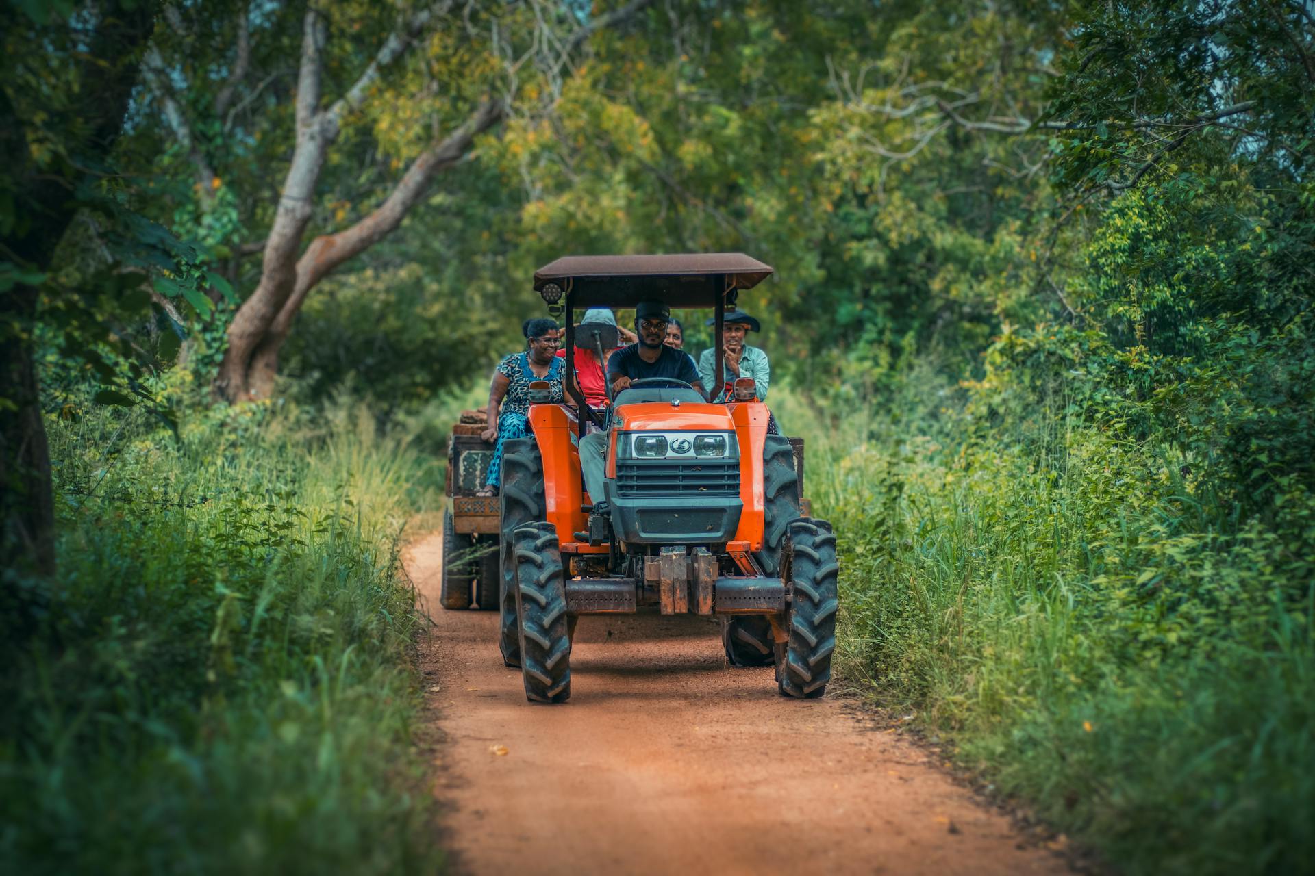 A Red Tractor with Farmers on a Trailer Driving on a Country Road