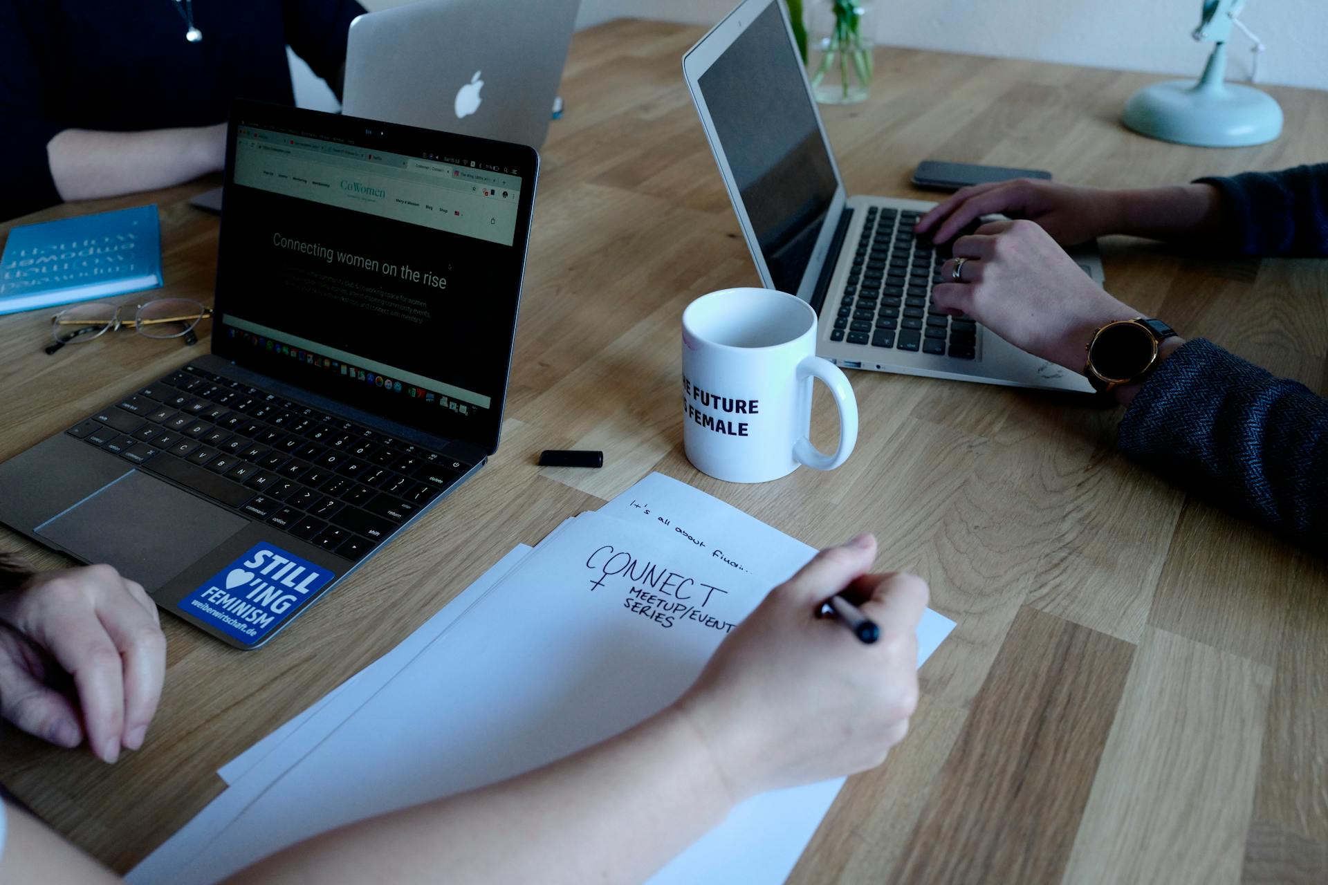 Team working with laptops and notes during a meeting at a wooden table.