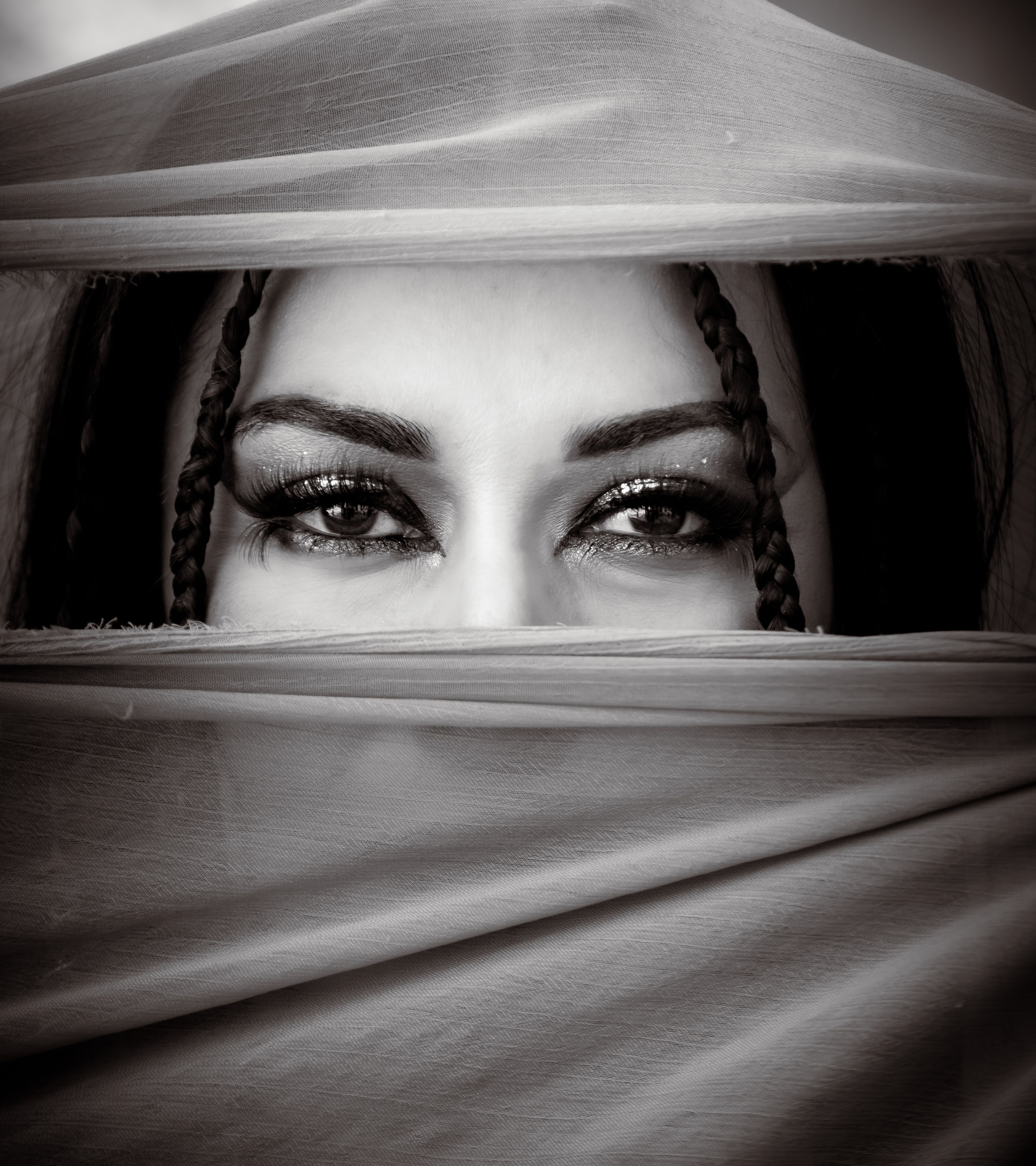 Captivating black and white portrait of eyes peeking through a veil, emphasizing mystery and allure.
