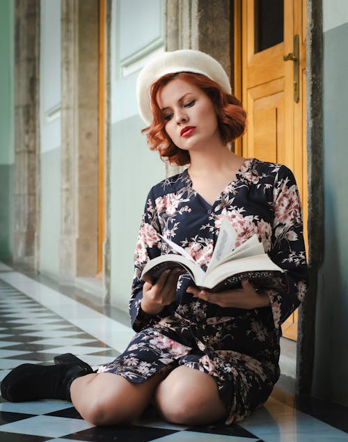 A woman in a hat and dress is reading a book