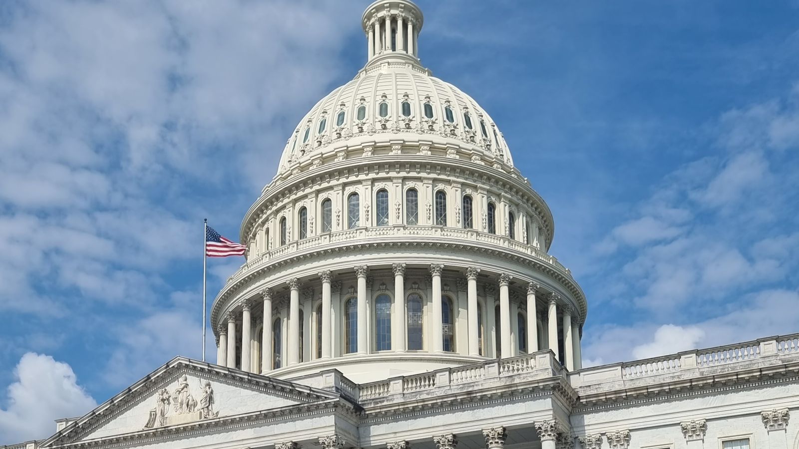 A striking view of the US Capitol dome with flag and blue sky in Washington, DC.