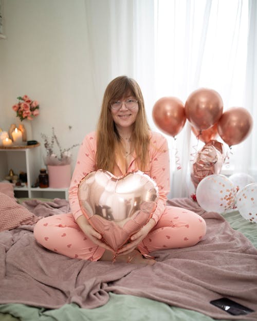 Smiling Woman in Pajama Sitting with Balloons on Bed