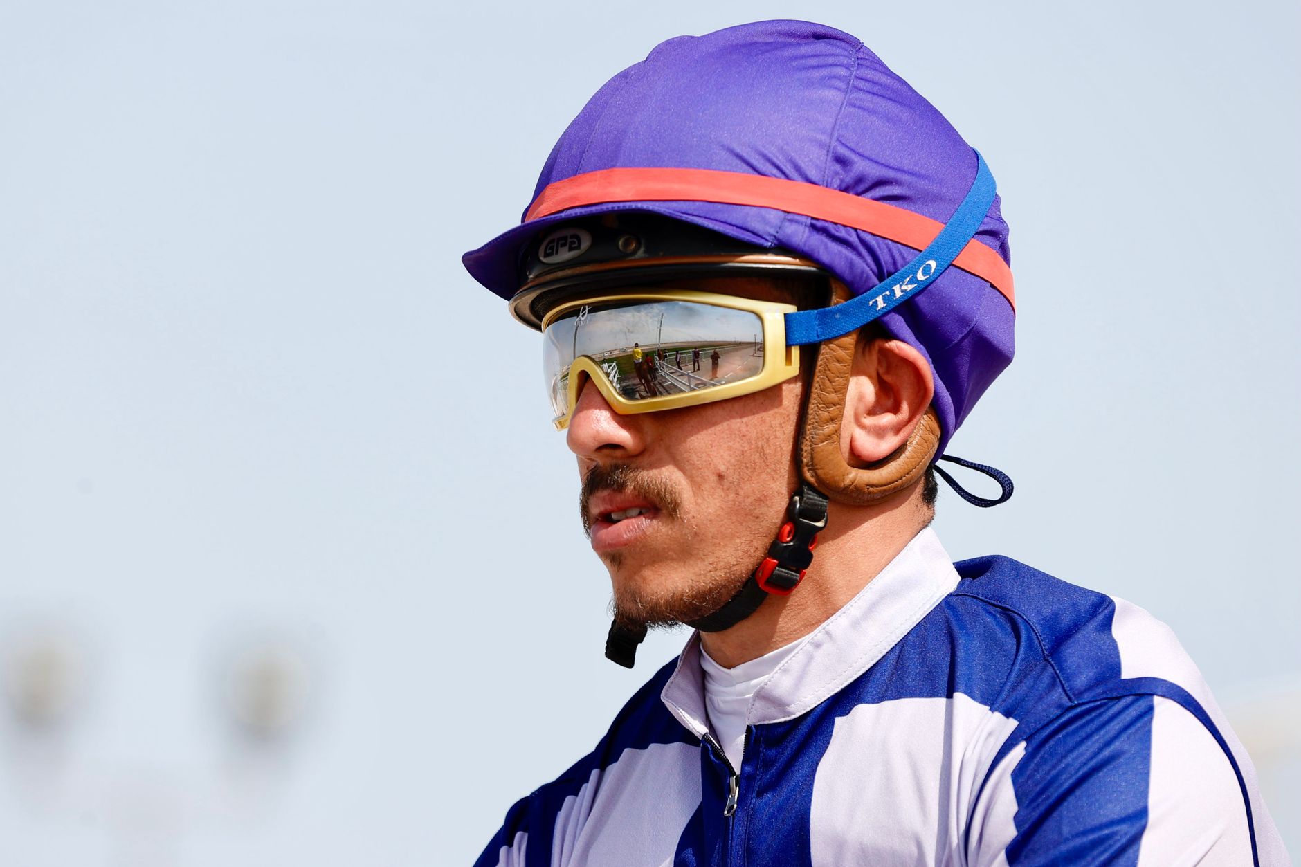Close-up of a jockey wearing a purple helmet and sunglasses at a racetrack.