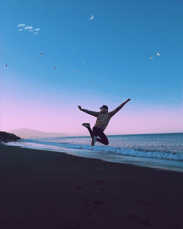 Free Man Jumping during Sunset on a Beach Stock Photo