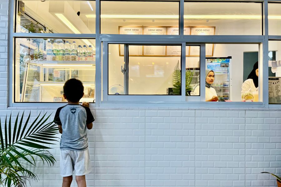 A young boy observes a café through the window, capturing a moment of curiosity in an urban setting.