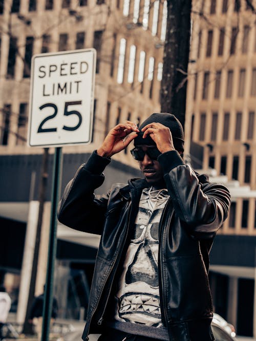 A man in a black jacket and sunglasses is looking at a speed limit sign