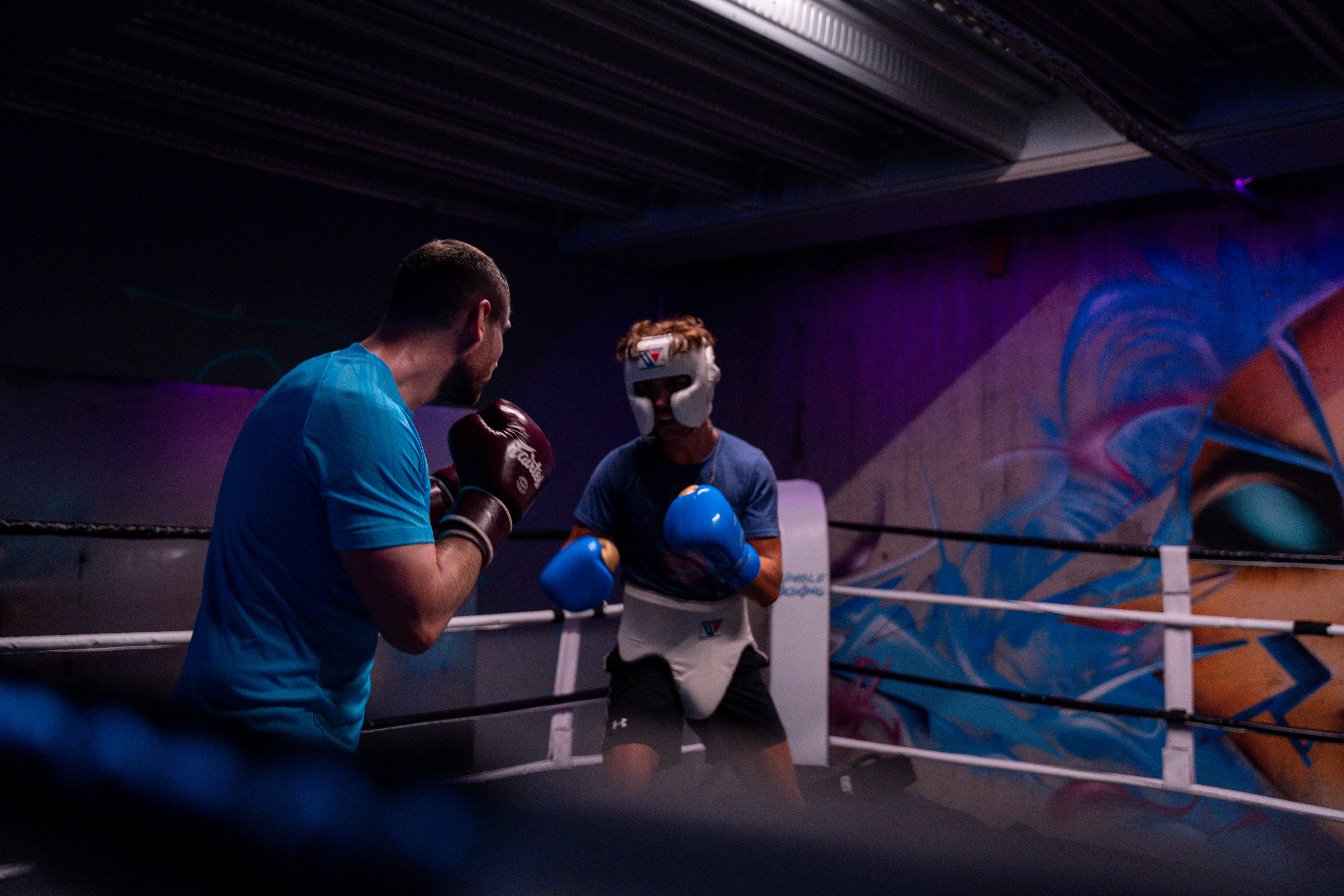Two male boxers engaged in training in an indoor boxing ring with colorful graffiti.