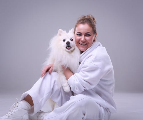 Smiling Woman in White Clothes Sitting and Hugging White Dog