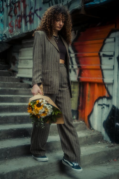 A woman in a suit and sneakers holding flowers