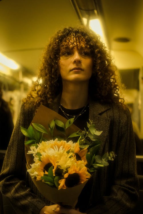 A woman with curly hair holding flowers on a train