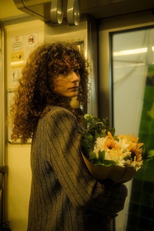 A woman with curly hair holding flowers in a train