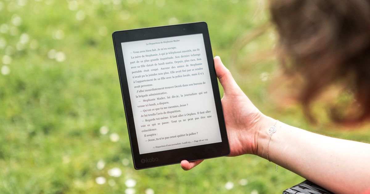 A hand holding an e-reader outdoors over a sunny lawn