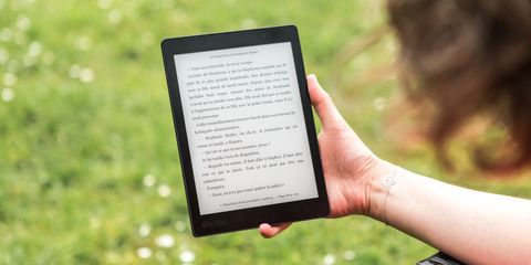 A hand holding an e-reader outdoors over a sunny lawn