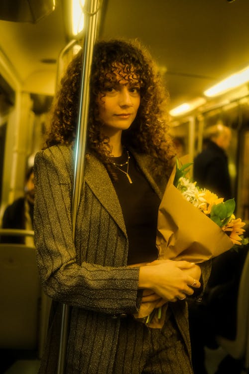 Woman with Curly Hair Standing with Flowers Bouquet on Metro Train