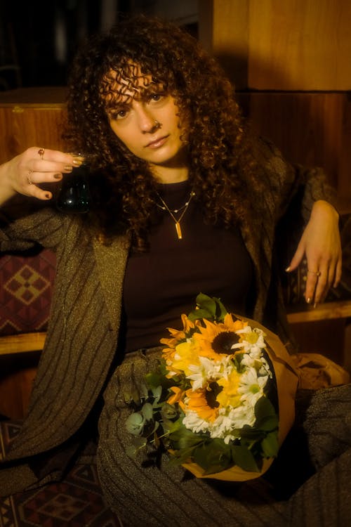 A woman sitting on a bench holding a flower and a cup