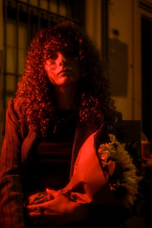 A woman with curly hair holding flowers in front of a red light