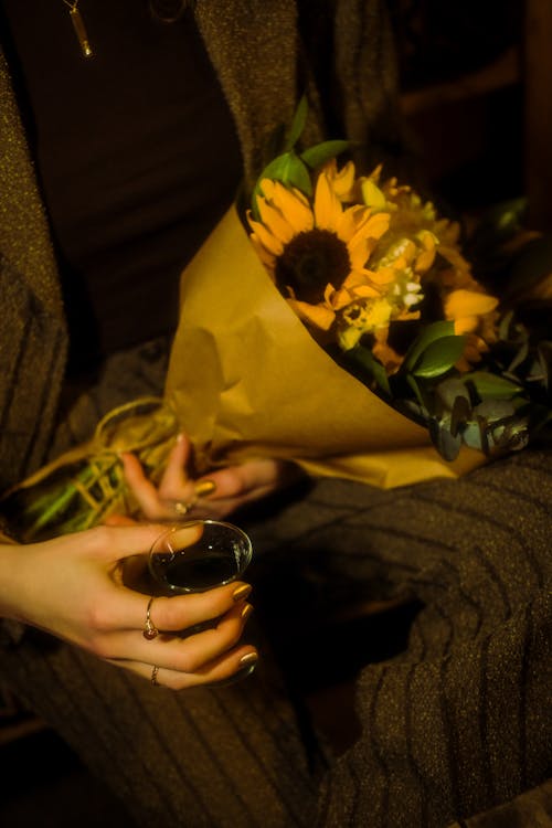 A woman holding a bouquet of sunflowers and a glass of wine